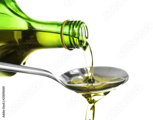 Pouring of olive oil from bottle into spoon on white background