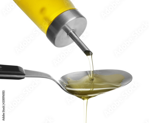 Pouring of olive oil from bottle into spoon on white background