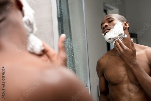 cropped shot of handsome african american man shaving and looking at mirror