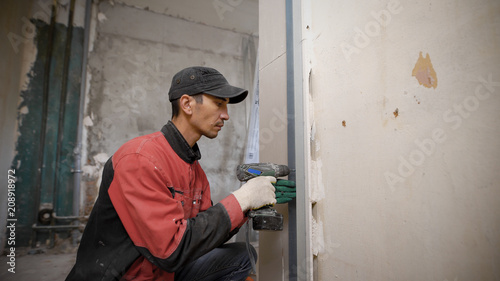 Man using tool fixing overlaps on wall in building