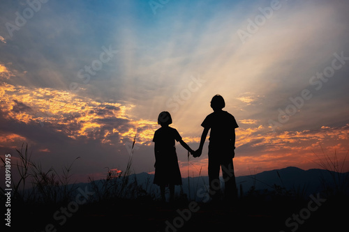 children silhouettes on summer meadow at sunset time