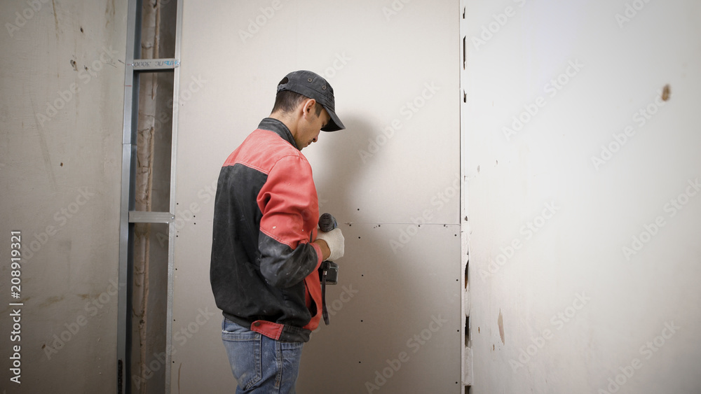 Construction worker is installing a new drywall in the apartment wearing uniform. Construction worker is installing a new drywall in the apartment wearing uniform.
