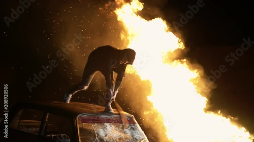 Revolution destructive behavior guy on the car with a baseball bat breaks glass. In the background is a fire. shooting at night