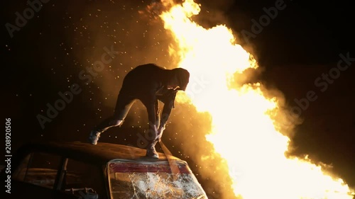 Revolution destructive behavior guy on the car with a baseball bat breaks glass. In the background is a fire. shooting at night photo