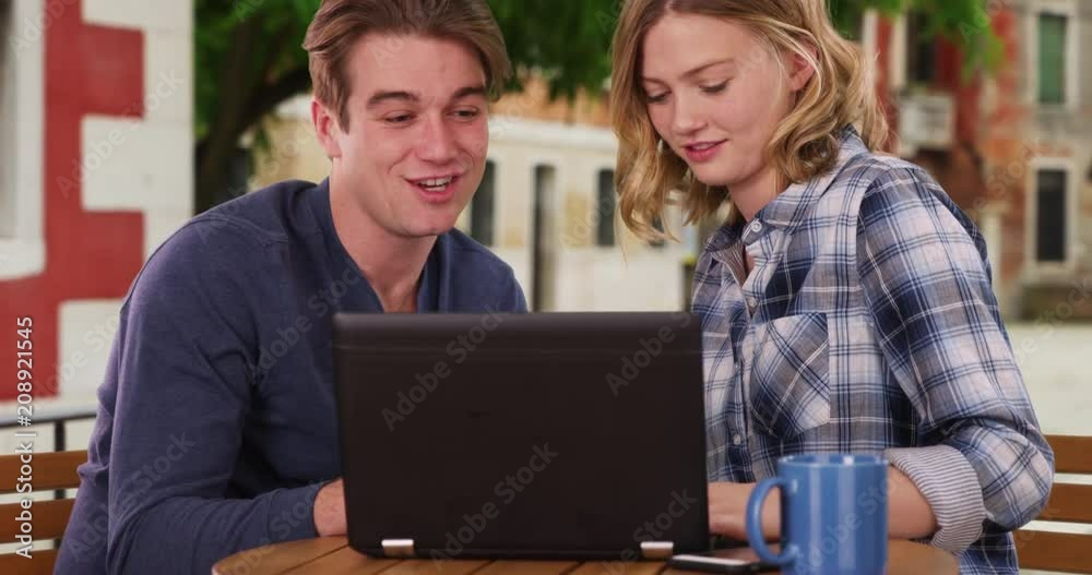 A Caucasian man and woman using laptop outdoors laughing, Portrait of millennial couple sitting outside using laptop, 4k A Caucasian man and woman using laptop outdoors laughing, Portrait of millennial couple sitting outside using laptop, 4k