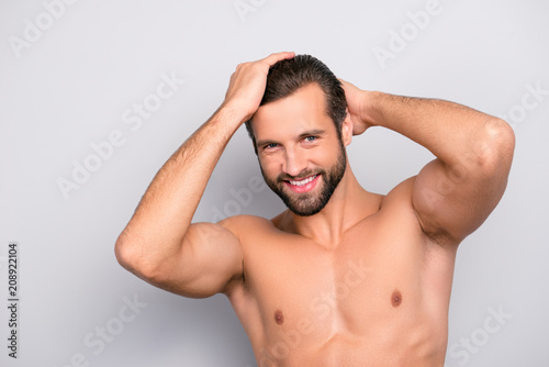 Attractive, harsh, virile, flirty, stunning, manly, confident, sportive macho with flawless, smooth, soft skin combing, touching his perfect hair with two hands, looking at camera over gray background