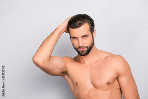 Attractive, harsh, virile, flirty, stunning, manly, confident, sportive macho with flawless, smooth, soft skin combing, touching his perfect hair with hand, looking at camera over gray background