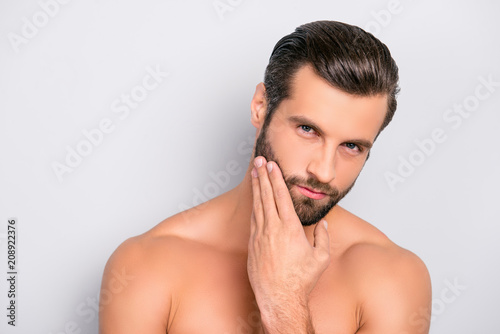 Attractive, brutal, modern, manly, virile, confident, dreamy, naked man touching his perfect, ideal face skin, holding hand on beard, cheek, looking at camera, isolated over gray background