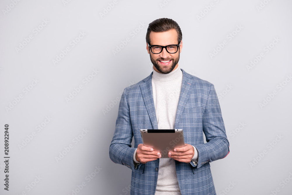 Portrait of virile, attractive, stunning man in glasses using, having tablet in hands, looking at camera, standing over gray background Portrait of virile, attractive, stunning man in glasses using, having tablet in hands, looking at camera, standing over gray background