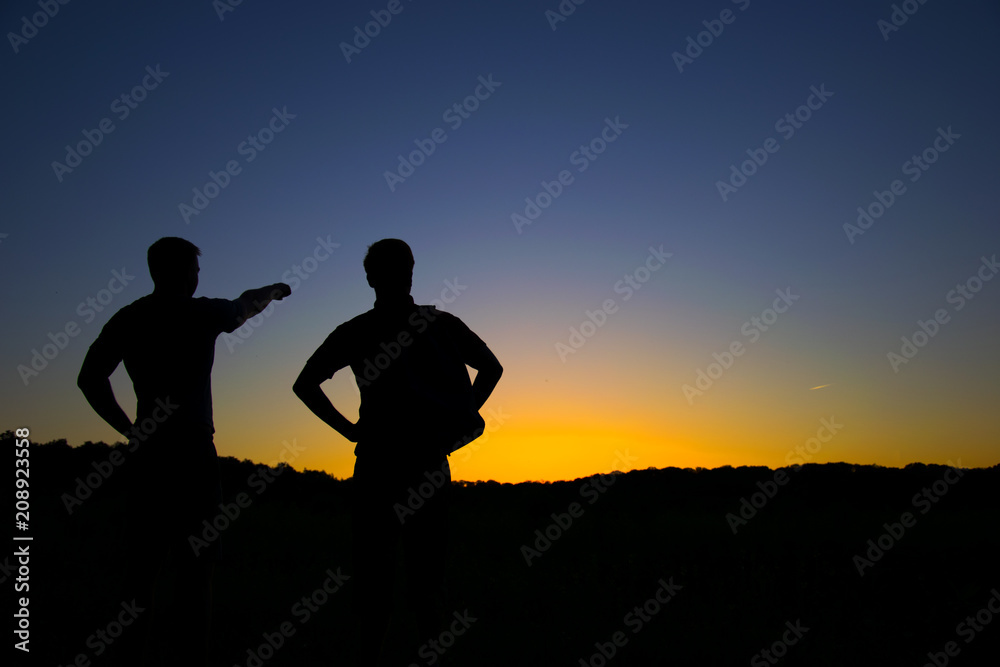 Silhouette of two men, One person shows a direction with his hand, against the background of the sunset. Tourism.