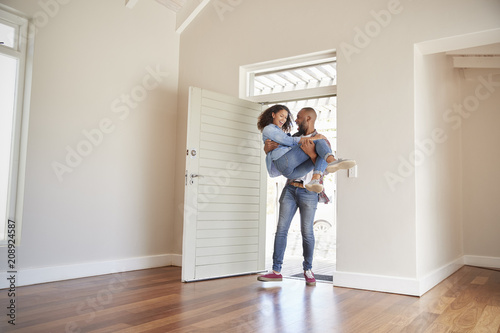 Man Carrying Woman Over Threshold Of Doorway In New Home