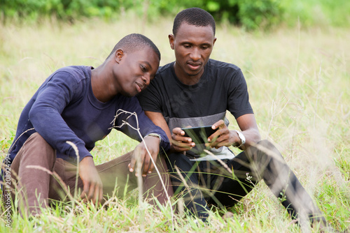 two young people using mobile phone sitting in the grass
