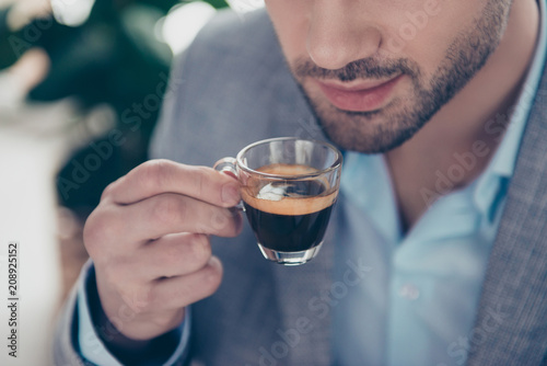 Cropped close up half face portrait of stylish attractive man holding small glass with espresso near mouth, every morning ritual before work in work place