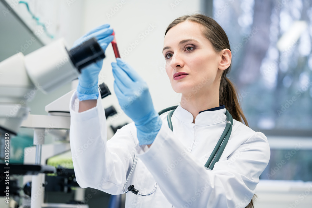 Doctor in medical laboratory looking at blood test she is holding in her hand Doctor in medical laboratory looking at blood test she is holding in her hand