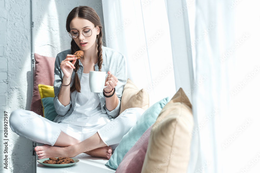 beautiful girl eating cookies with coffee on windowsill with pillows beautiful girl eating cookies with coffee on windowsill with pillows