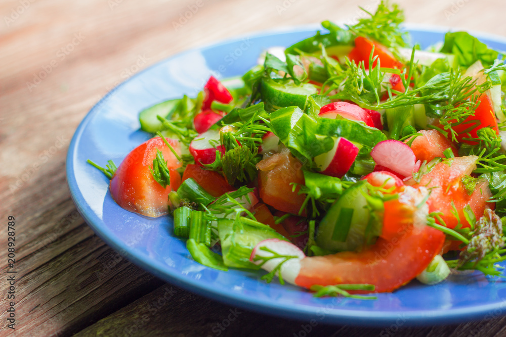 salad of fresh vegetables and greens in a plate on a wooden background