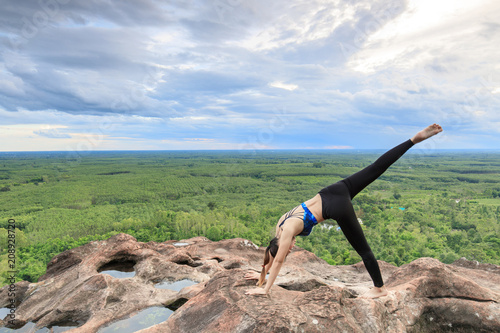 Asian women play it yoga on the mountain rock cliff.