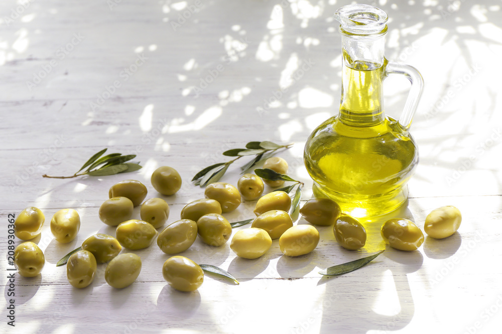 Glass jug with fresh oil and canned olives on wooden table Glass jug with fresh oil and canned olives on wooden table