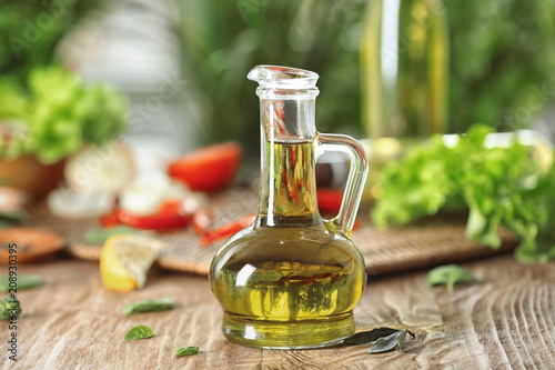 Glass jug with fresh olive oil on wooden table