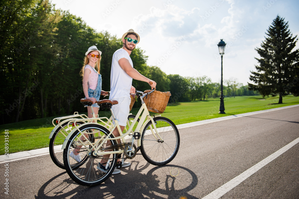 Obraz premium Portrait of trendy stylish brother and sister with retro bikes after riding walking in forest looking at camera. Fresh air green grass trees perfect weather idyllic atmosphere concept