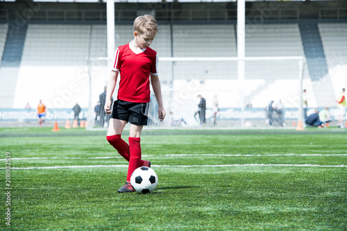 Full length portrait of teenage boy leading ball while playing football during practice in outdoor stadium, copy space