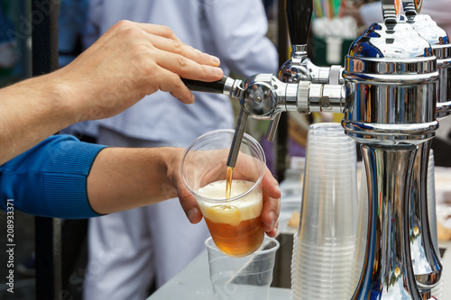 barman s hand holds a large glass in which fresh amber beer is poured with foam. Street trading