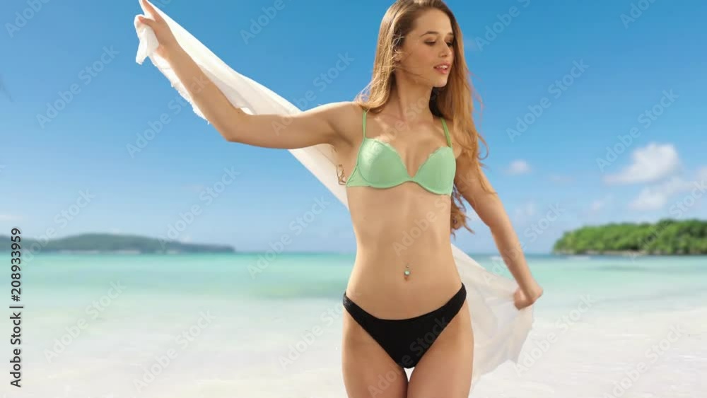 blonde woman with long hair wearing a bikini turning and playing with a sorong on a tropical beach blonde woman with long hair wearing a bikini turning and playing with a sorong on a tropical beach