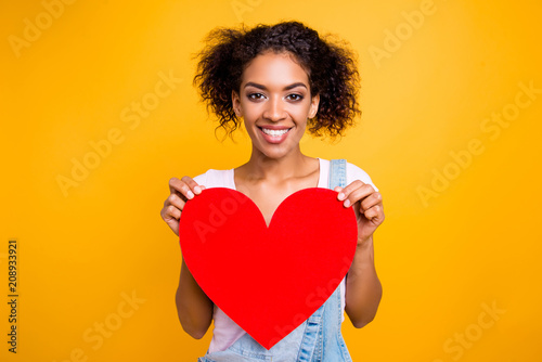 Portrait of cheerful toothy girl with beaming smile having big carton paper heart in hands looking at camera isolated on yellow background. Rest relax leisure concept