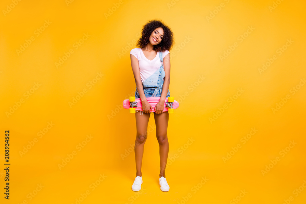 Full size portrait of funky cute coquette holding pink skate board in hands looking at camera isolated on yellow background. Urban outside outdoor street style concept Full size portrait of funky cute coquette holding pink skate board in hands looking at camera isolated on yellow background. Urban outside outdoor street style concept