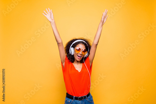 Portrait of cheerful positive chic holding raised arms having headphones on head listening music singing song enjoying weekend vacation isolated on yellow background