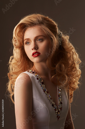 Fashion beauty studio portrait of young beautiful pretty woman with makeup, red lips and updo hairstyling. Stunning girl with golden hair. Photo in warm colors.