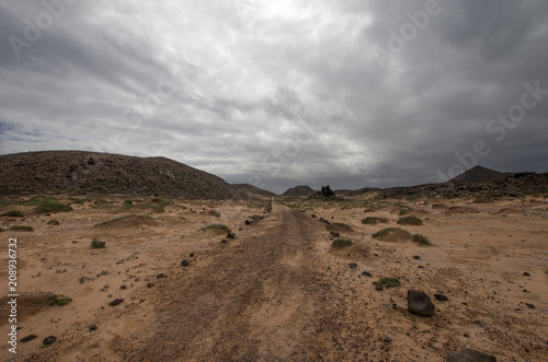 desert trail just dashed and punctuated by lava rocks under a stormy sky.fuerteventura  spain