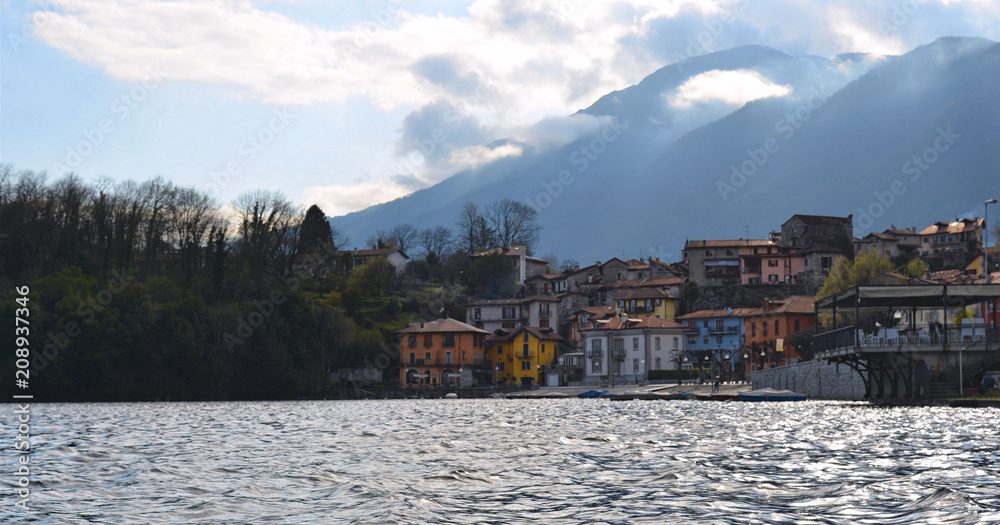 Cloudy blue sky with mountains and old small village with colorful buildings on lake Mergozzo in Piemont, Italy Cloudy blue sky with mountains and old small village with colorful buildings on lake Mergozzo in Piemont, Italy
