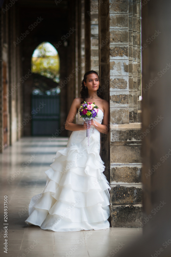The bride in the gallery of stone walls in a beautiful white wedding dress with a bouquet of flowers The bride in the gallery of stone walls in a beautiful white wedding dress with a bouquet of flowers