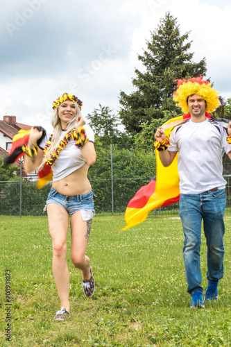 Männlicher und weiblicher Fussballfan auf Wiese glücklich über den Sieg der deutschen Nationalmannschaft