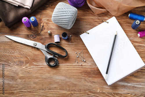 Notebook and sewing accessories on wooden background