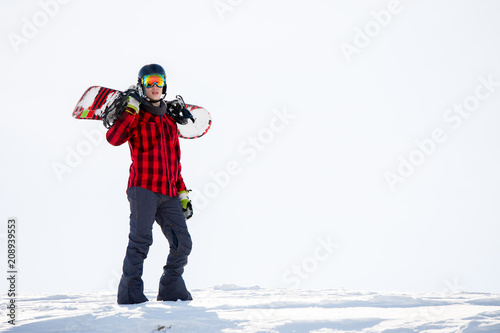 Photo of man with snowboard on shoulders standing on snowy mountainside