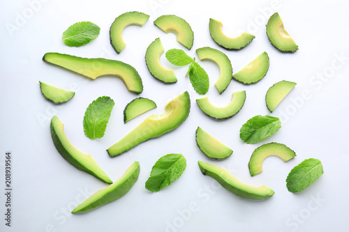 Slices of ripe avocado with mint leaves on white background