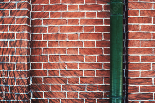 Hallucinogen red surreal brick wall with green downspout. Asymmetric angle of exotic brown fluorescent uneven wall in perspective. Haunted imagination from drugs and alcohol. Drain pipe is in right.