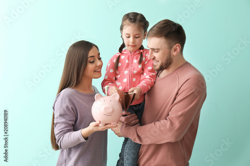 Happy young family with piggy bank, wallet and money on color background