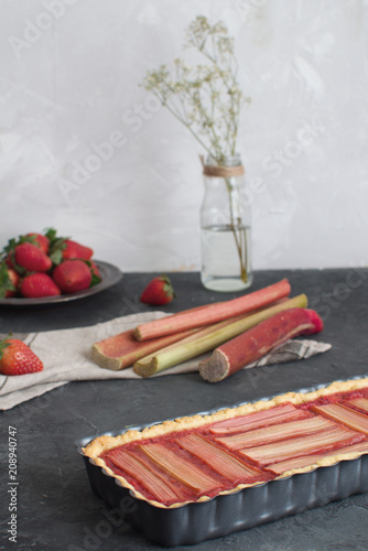 Scene with fresh baked rhubarb cake and fresh rhubarb and strawberries on the background