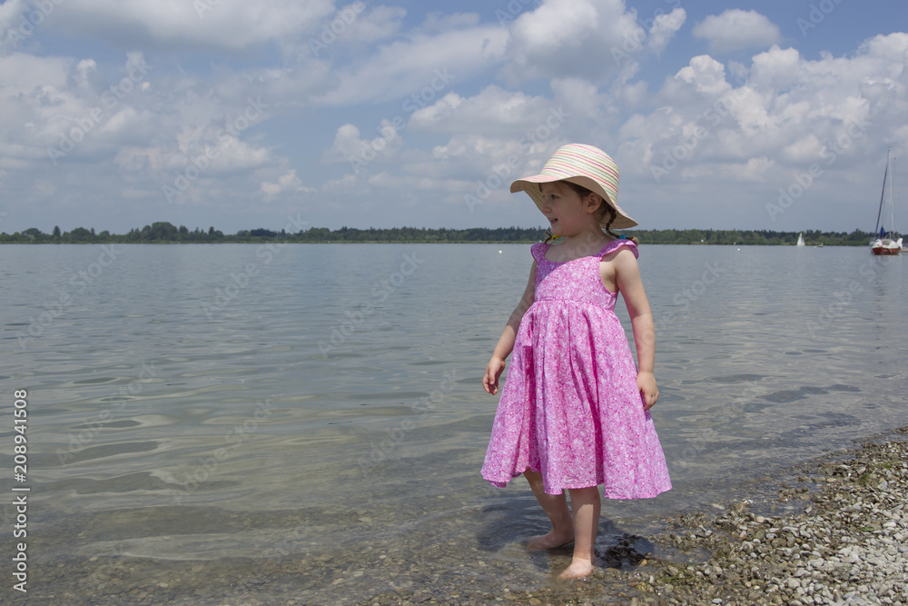 A little girl wearing a sunhat is walking in the water