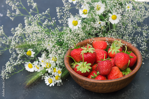 Fototapeta Naklejka Na Ścianę i Meble -  red strawberry in a clay cup with flowers gypsophila daisy field on a dark background