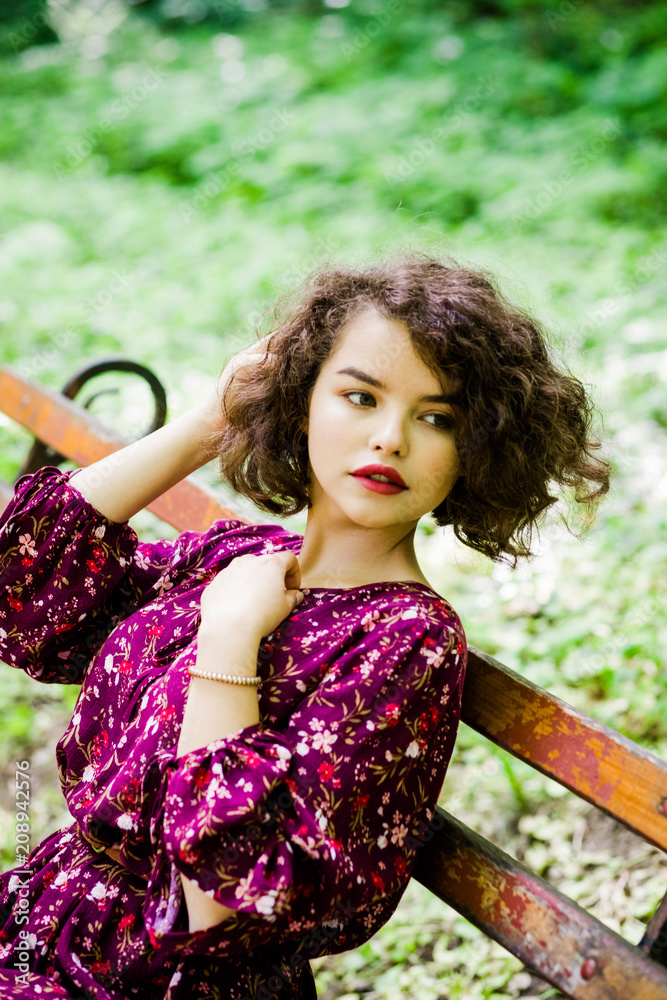 Naklejka premium A wonderful girl in a purple dress, sitting on a bench in the park