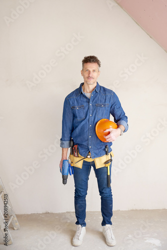 Smiling mature construction man portrait with handyman belt and safety helmet and drill