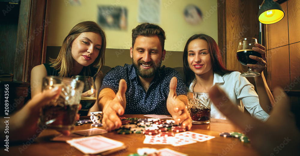 Fototapeta premium Side view photo of friends sitting at wooden table. Friends having fun while playing board game.