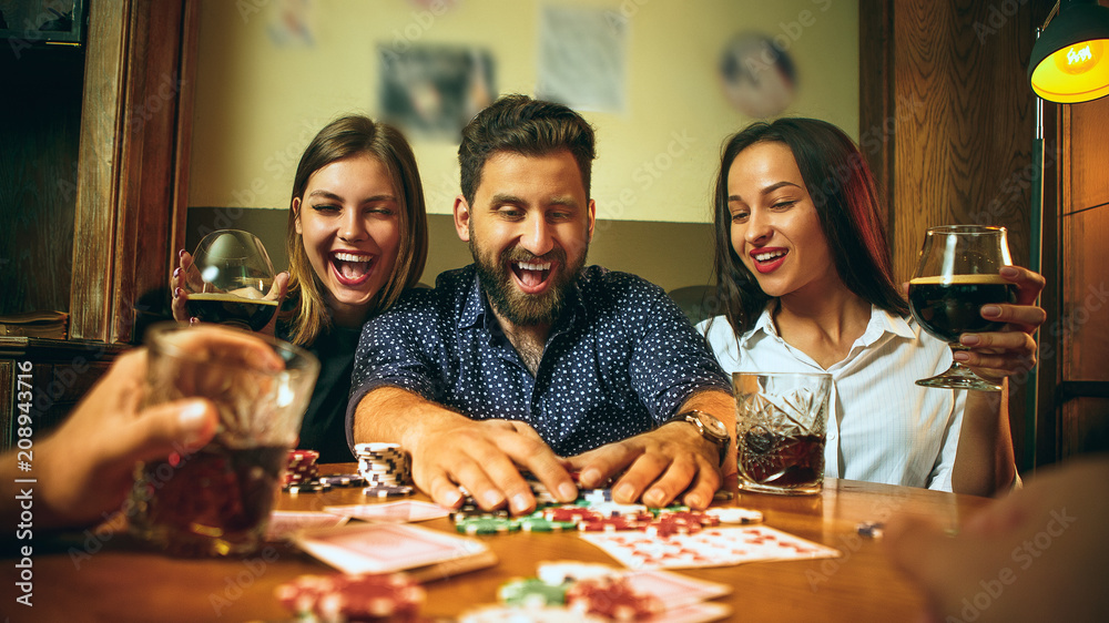 Fototapeta premium Side view photo of friends sitting at wooden table. Friends having fun while playing board game.