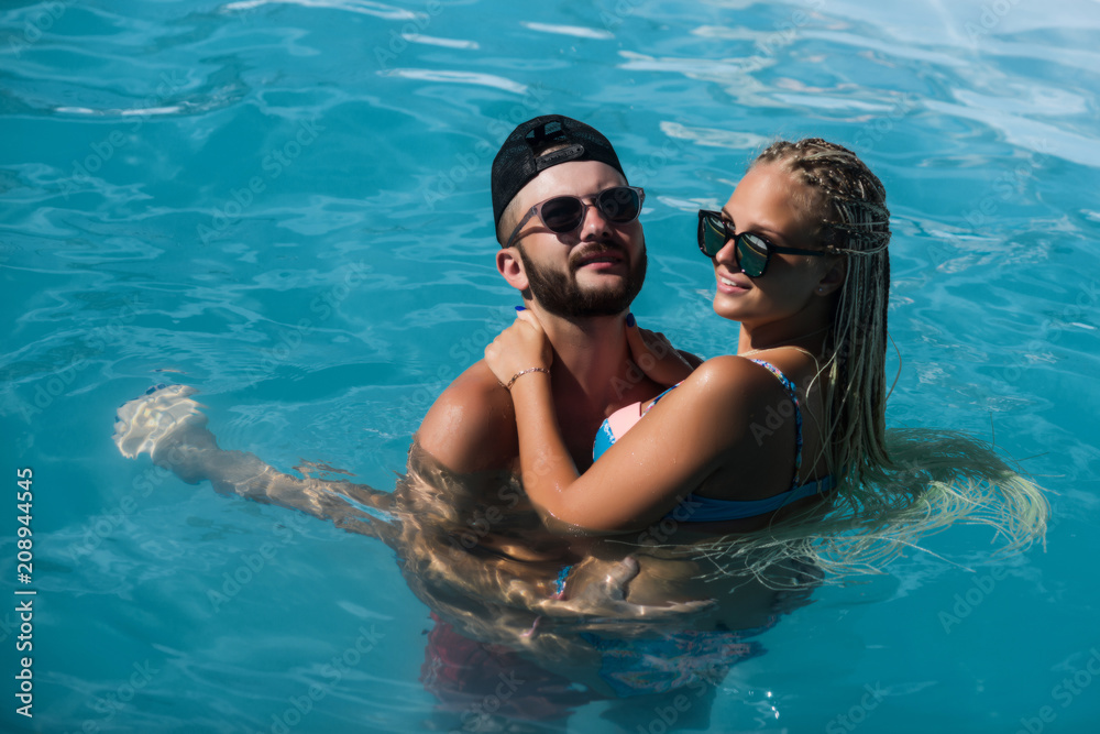 A man in a black cap and a woman in sunglasses and a sexy blue swimsuit are swimming in the water. Couple swimming in the pool. The concept of rest