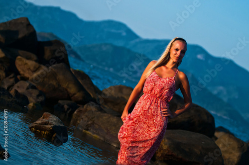 Sexy girl posing at sunset on a background of stones, mountains and the sea