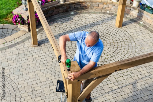 Tableau sur toile Man building a wooden gazebo on a brick patio